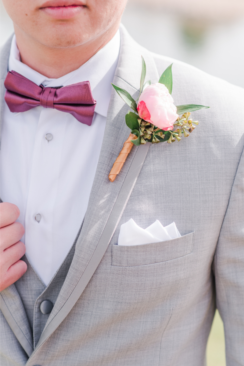 Groom holds edge of suit as photographer captures his pink boutonniere.