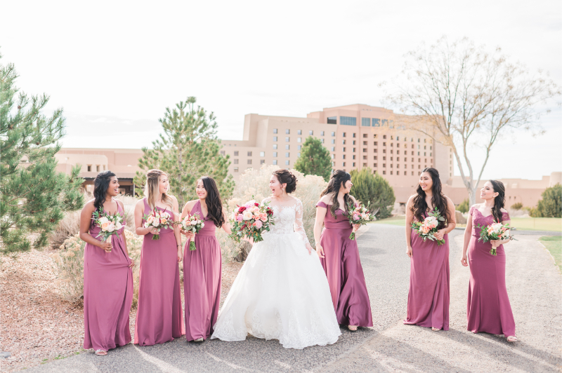 Bride walks ahead of bridesmaids as she looks back at them and smiles for photos.