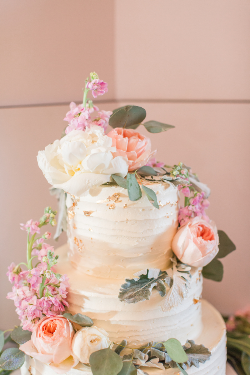 Three-tired white cake decorated with florals for a pink and green wedding.