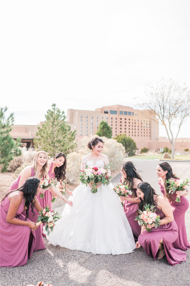 Bridesmaids in pink dresses circle bride to fluff her dress.