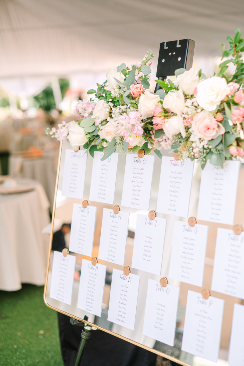 Seating chart for tented wedding decorated with a floral arrangement at the top of the easel.